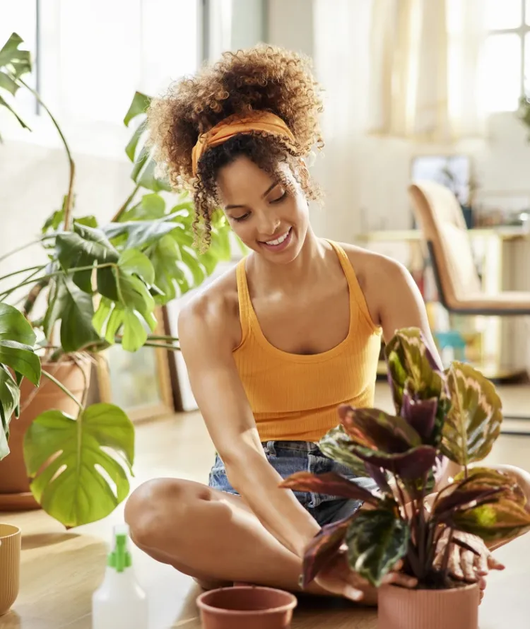 Mulher de cabelo cacheado sorrindo e mexendo em planta