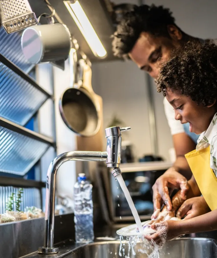 Pai e filho lavando louça em cozinha de casa 